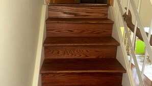 A wooden staircase with a white railing leading to a bedroom with a bed.