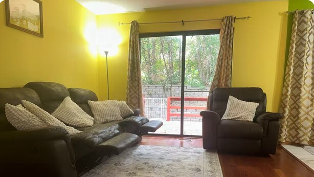 A living room with a black leather sofa, a matching armchair, and a patterned rug.
