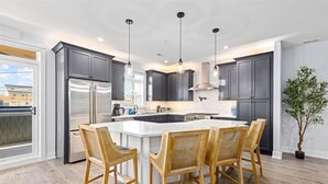 Una cocina moderna con armarios oscuros, electrodomésticos de acero inoxidable, una isla central con sillas e iluminación colgante.