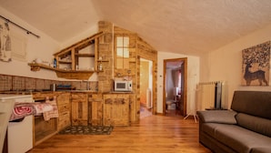 Une cuisine rustique avec des meubles en bois et un mur en pierre, qui donne sur une salle de bain et un espace de vie avec un canapé.