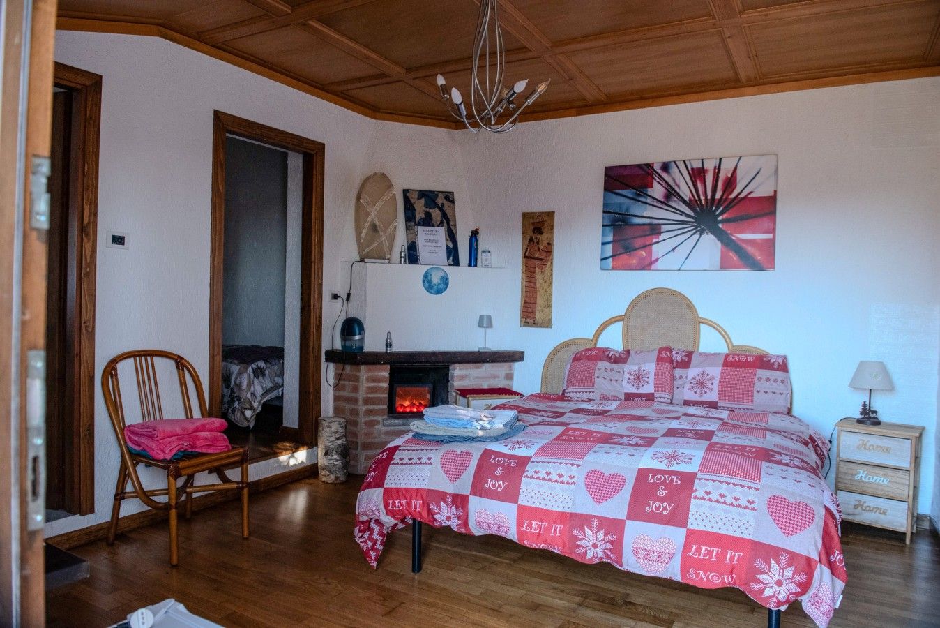 A bedroom with a bed, a chair, a fireplace, and a wall with artwork.