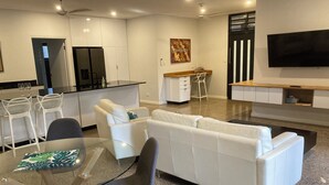 A modern living room with a white sofa, a glass coffee table, and a dining area with white chairs. - 1BR (sleeps 3) - private, modern granny flat with large shaded pool (Parap)