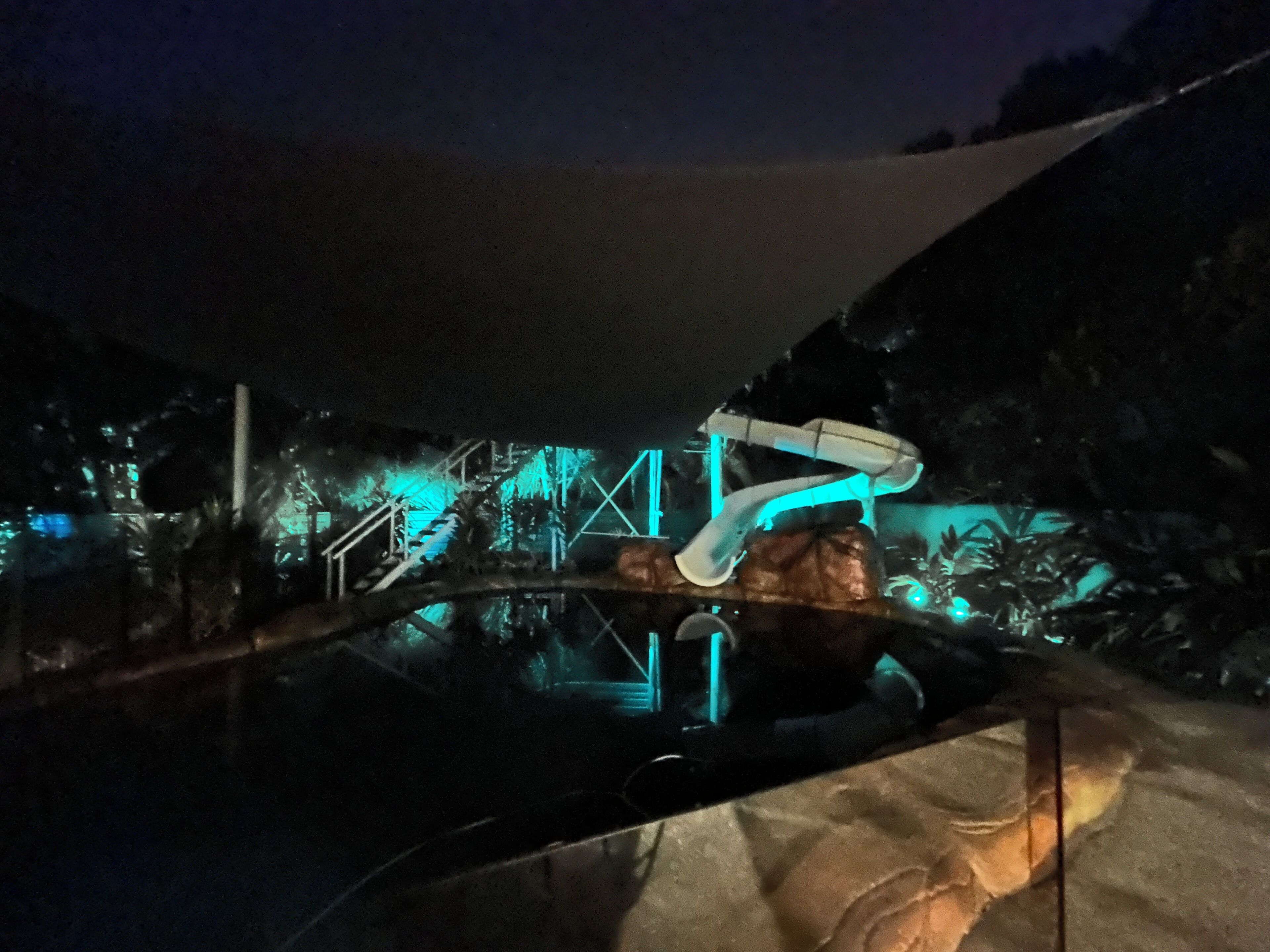 A nighttime view of a pool area with a large rock formation and a canopy overhead.