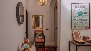 Un couloir orné d’un lustre, d’un miroir, d’une affiche encadrée avec une citation, d’une chaise et d’une petite table sur laquelle se trouve un plateau de pâtisseries.