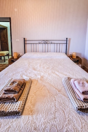 A neatly made bed with a patterned bedspread, two side tables with candles, and a mirror on the wall.