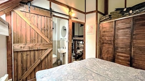 A bedroom with a wooden door, a bed with a patterned bedspread, and a wardrobe.