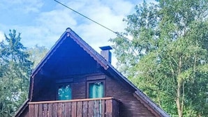 A two-story house with a wooden balcony, a patio with outdoor furniture, and a fenced yard.