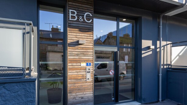 Ein Gebäudeeingang mit Holzpaneelen, einer Glastür und einem Schild mit der Aufschrift "B&C".