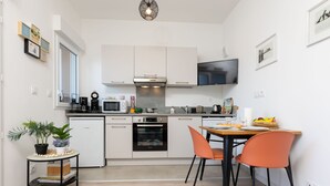 Eine moderne Küche mit weißen Schränken, einer Mikrowelle, einem Backofen und einem Essbereich mit orangefarbenen Stühlen.