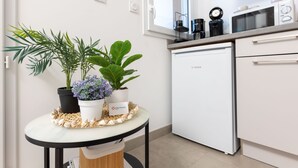 Eine kompakte Küche mit einem Bosch-Kühlschrank, einer Mikrowelle und einer Kaffeemaschine auf der Arbeitsplatte. Es ist ein kleiner runder Tisch mit Topfpflanzen und einer dekorativen Muschelschale.