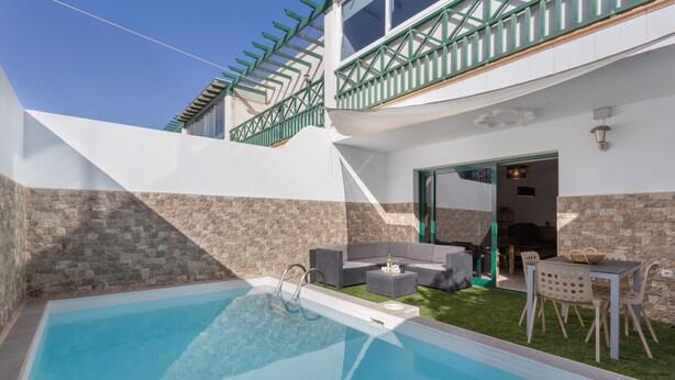 Una piscina con pared de piedra, mobiliario de exterior y un patio cubierto.