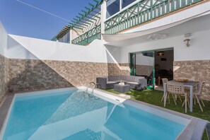 Une piscine bordée d’un muret en pierre, avec un espace extérieur aménagé pour s’asseoir et une terrasse couverte.