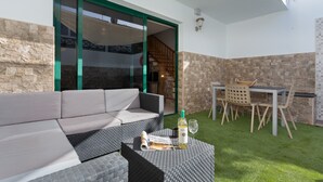 Un patio con un sofá, una mesa con sillas, una botella de vino y una revista.