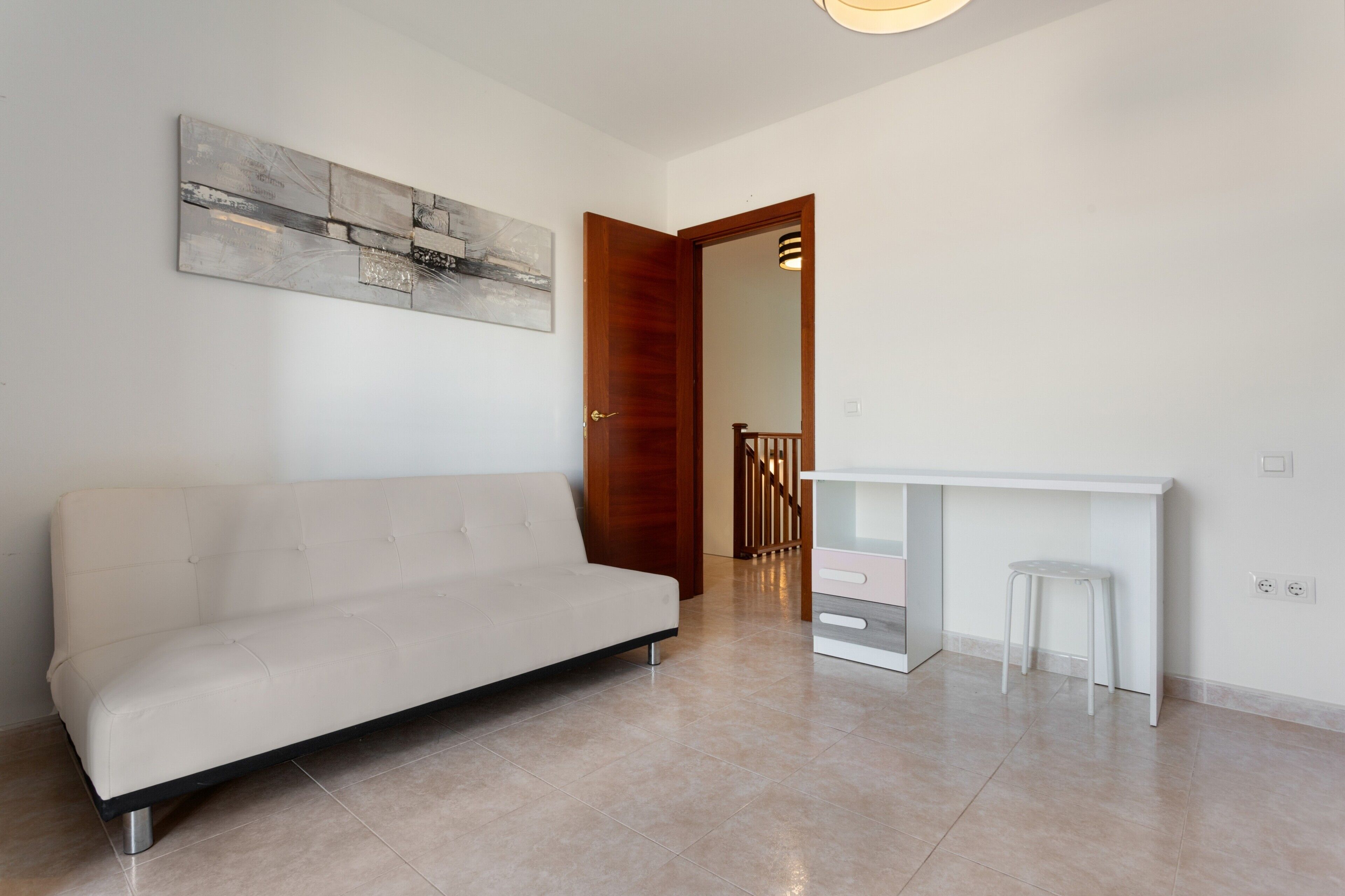 Un salon moderne avec un canapé, un bureau blanc et un escalier menant à une autre pièce.