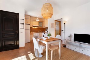 Una cucina moderna con mobili bianchi, un tavolo da pranzo con sedie, una televisione e un'ampia porta scura.