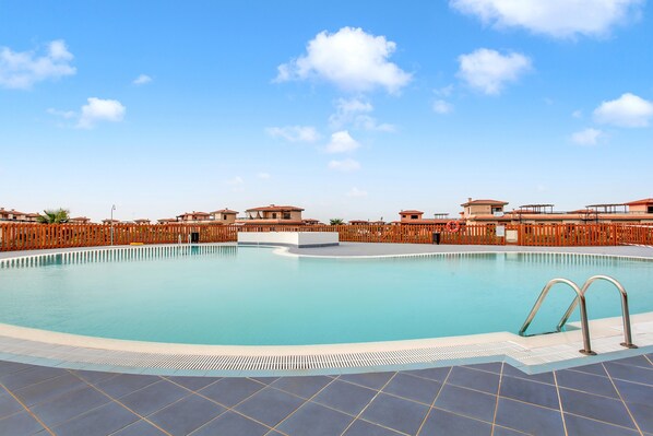 A swimming pool with a wooden fence, clear blue sky, and buildings in the background.