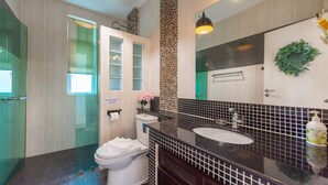 Un baño moderno con cabina de ducha de vidrio, un inodoro, un lavamanos con espejo y una guirnalda decorativa en la pared.
