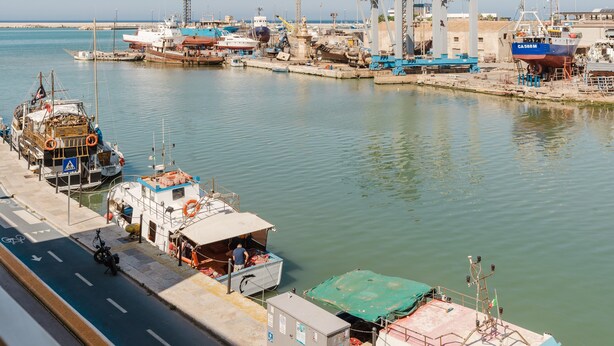 Un port où des bateaux sont amarrés, une route qui longe le port et, au loin, des bâtiments industriels.