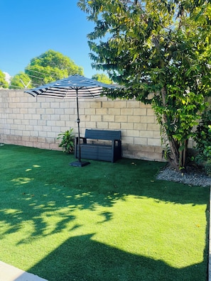 A well-maintained lawn with a bench and a striped umbrella.
