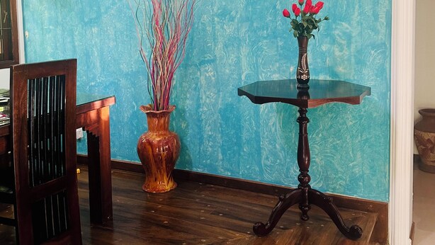 A room with a teal textured wall, a wooden dining table, a vase with red flowers, and a tall vase with branches. - Villa Gajeru Walawwa by W Lanka (Balapitiya)