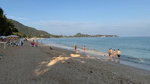 A beach with sun loungers, umbrellas, and people enjoying the water. - Amazing new 1-bedroom apartment, fabulous Lamai Beach,  swimming pool, fitness (Koh Samui)