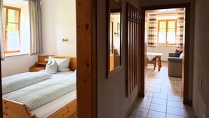 Quarto com duas camas, um guarda-roupa de madeira, um espelho e vista para uma sala de jantar.