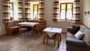 Uma área de refeições acolhedora com mesa e cadeiras de madeira, um banco e cortinas listradas.