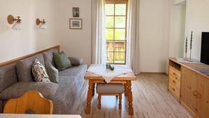 Uma sala de estar acolhedora com um sofá de madeira, uma mesa pequena de madeira com toalha de renda e uma TV em um armário de madeira.