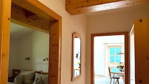 Ein Flur, der in einen Essbereich mit Tisch und Stühlen führt, mit Holzboden und einer Couch mit Kissen.