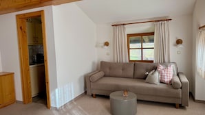 Ein gemütliches Wohnzimmer mit einer Couch, einem kleinen runden Tisch und einer durch einen offenen Durchgang sichtbaren Küche.