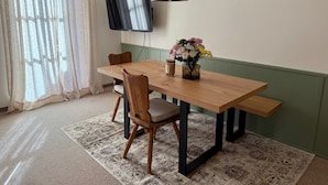 Ein Essbereich mit einem Holztisch, Stühlen, einem Blumenstrauß, einem Fernseher und gerahmten Bildern an der Wand.