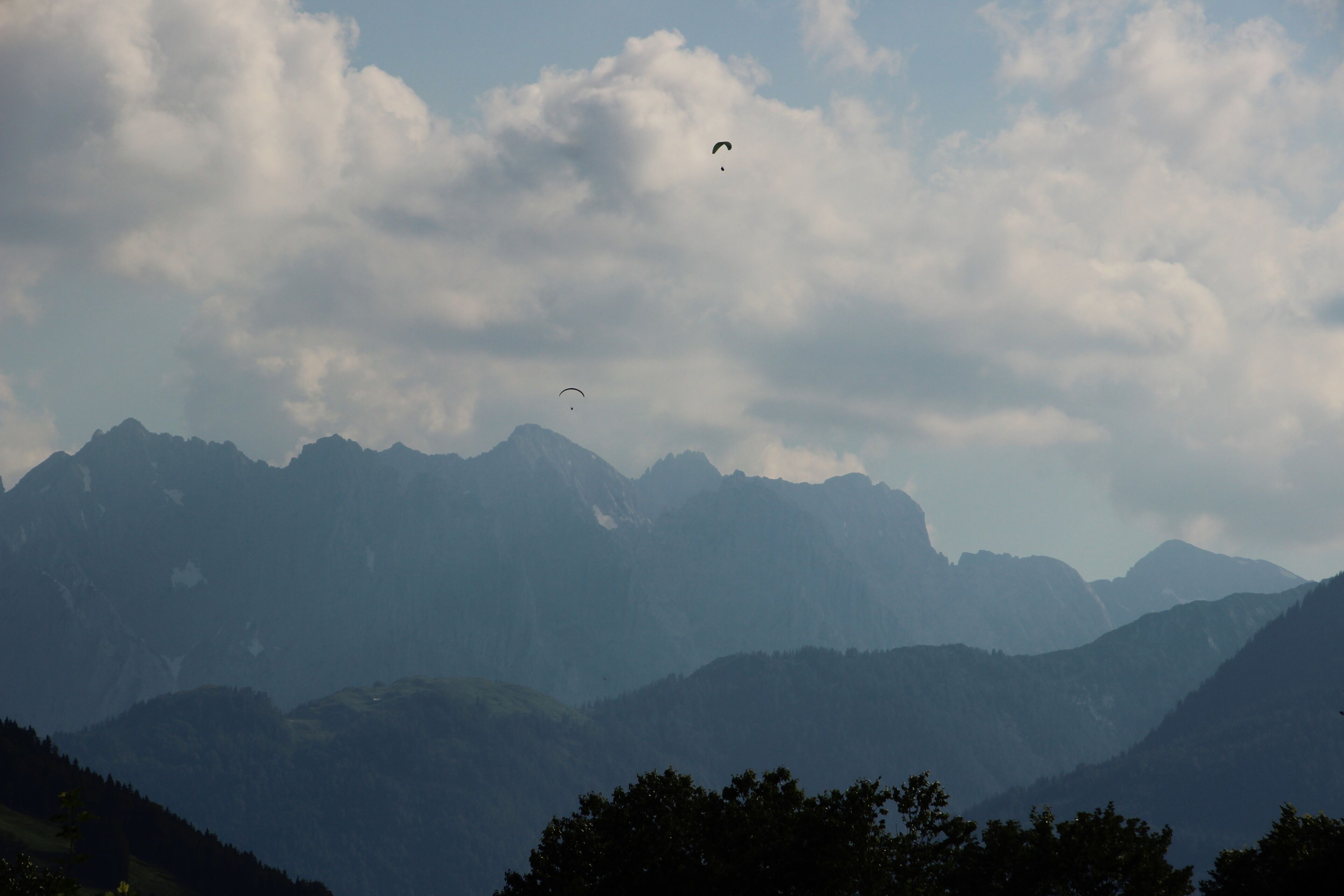 A mountainous landscape with two paragliders in the sky.