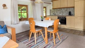 Eine kleine Küche mit Holzschränken, einem Esstisch mit Stühlen und einem kleinen Fenster mit Vorhängen.