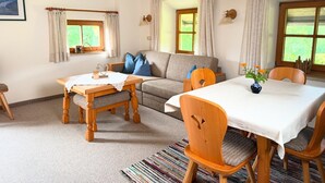 Ein gemütliches Wohnzimmer mit einer Couch, einem Esstisch mit Stühlen und einem Fenster mit Vorhängen.