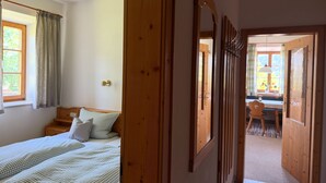 Ein Schlafzimmer mit einem Bett, einem Holzschrank, einem Spiegel und einem Fenster mit Vorhängen.