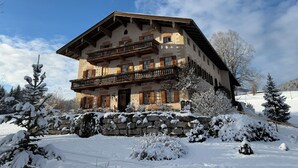 Ein mehrstöckiges Chalet mit Steinverkleidung, Holzbalkonen und verschneiter Landschaft.