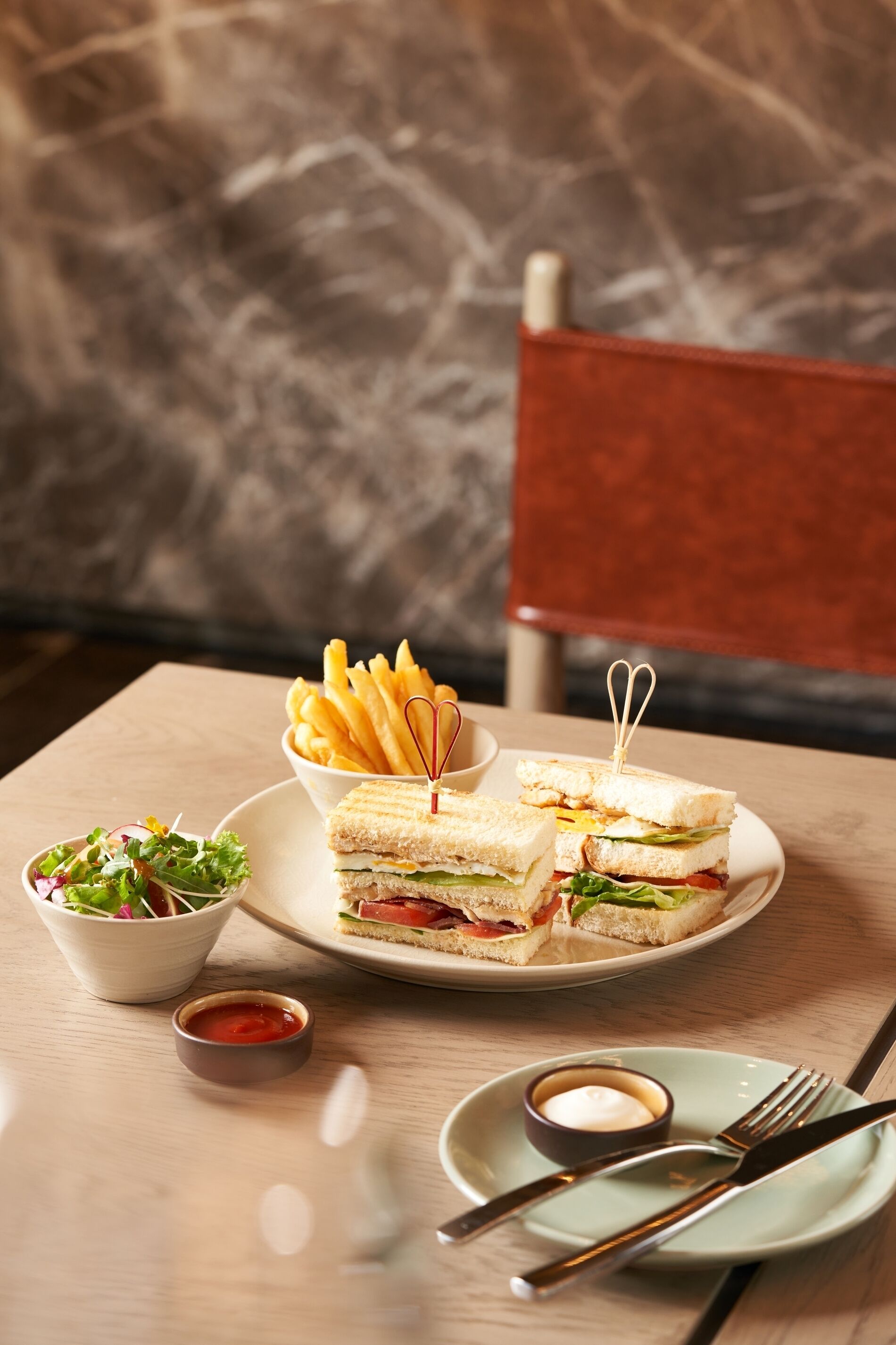 A table with a sandwich, fries, salad, and condiments.