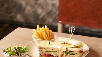 Una mesa con un sándwich, papas fritas, ensalada y salsas.