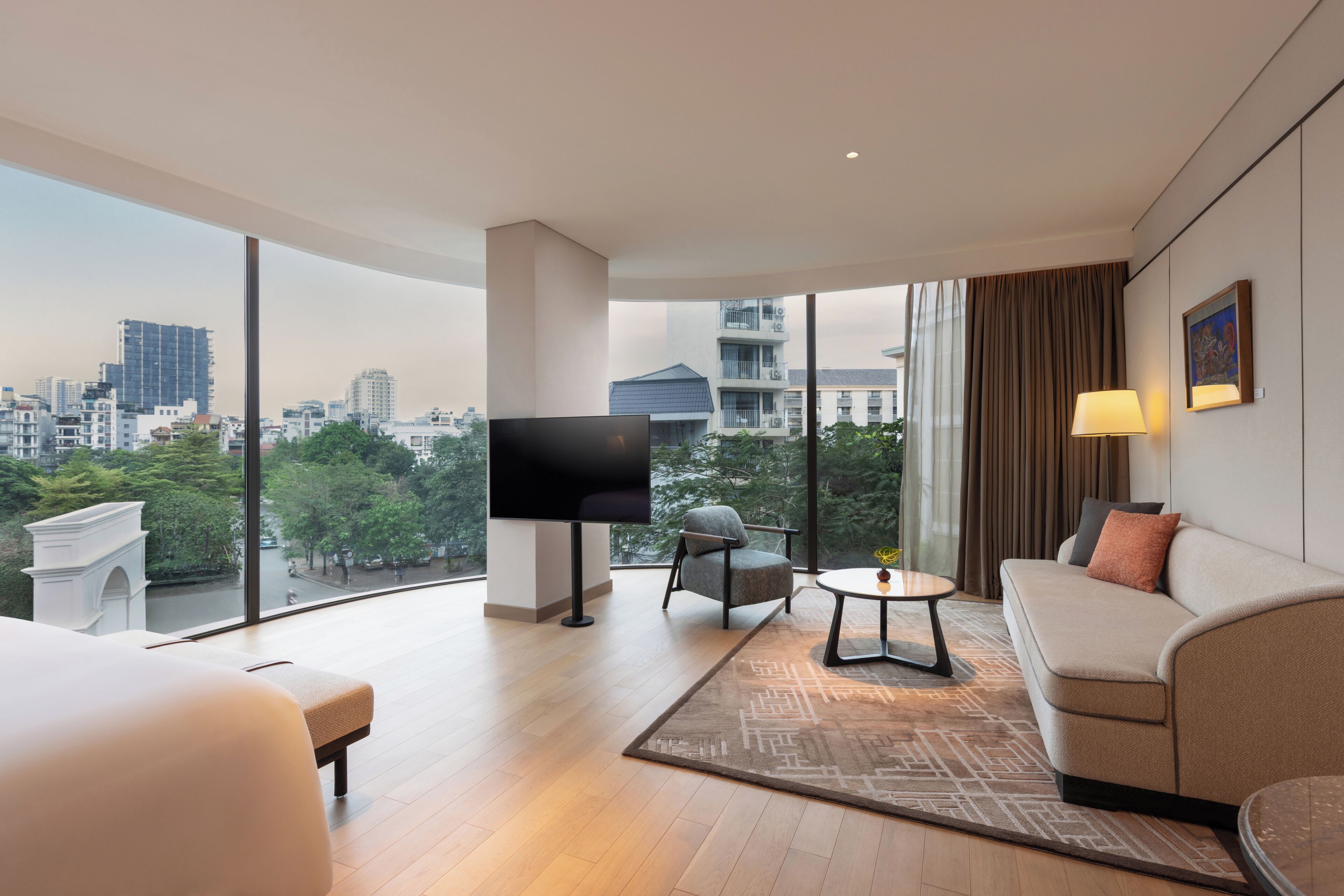Een moderne hotelkamer met een groot raam, een flatscreen televisie, een bank, een stoel en een klein tafeltje.