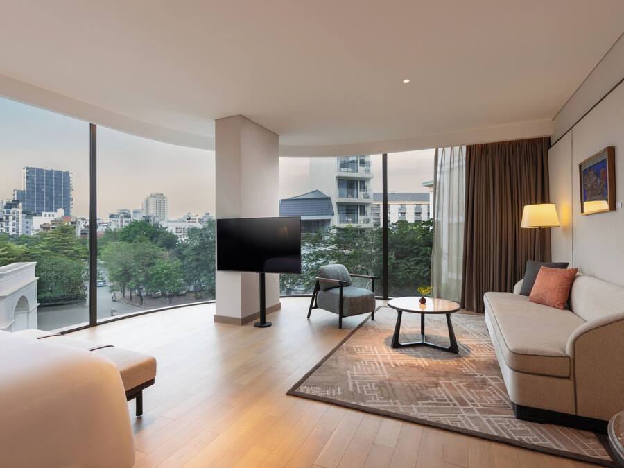 Een moderne hotelkamer met een groot raam, een flatscreen televisie, een bank, een stoel en een klein tafeltje.