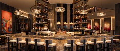 A bar area with a circular bar, multiple high chairs, and a large chandelier.