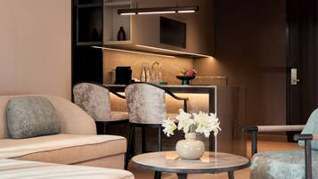 A modern living room with a sofa, a round table with a vase of flowers, and a kitchen area in the background.