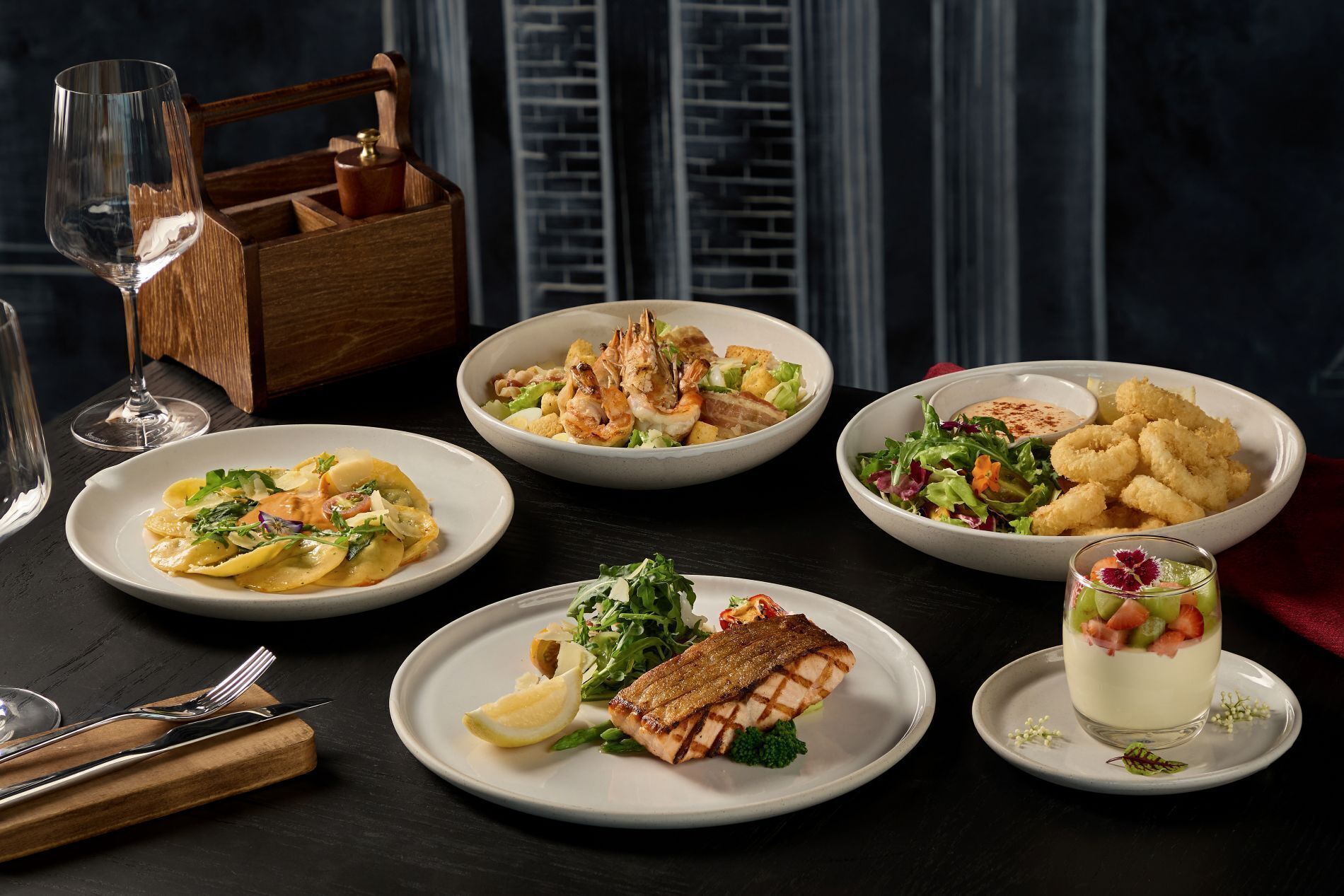 Una mesa servida con diversos platos, incluyendo mariscos, ensaladas y un postre, con copas de vino y cubiertos.