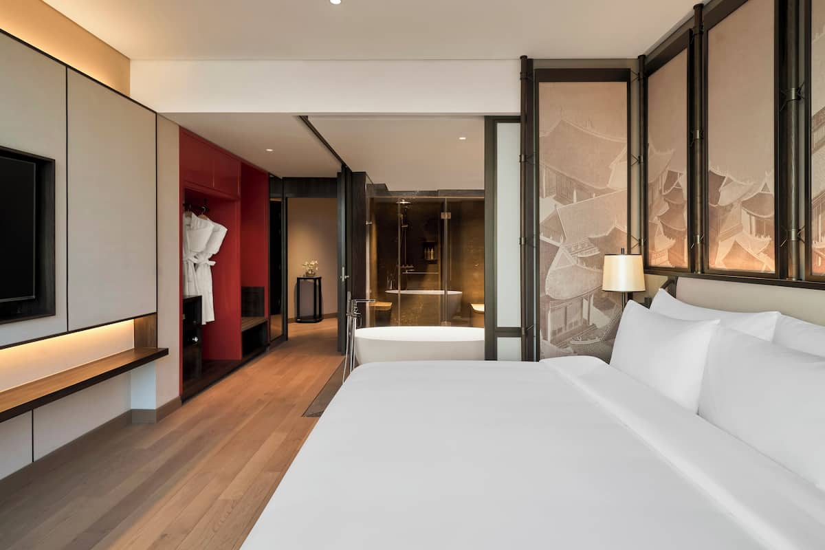 Une chambre d’hôtel moderne avec un grand lit, une télévision, une armoire rouge et une salle de bain avec baignoire.