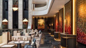 Een ruime lobby met een hoge plafond, moderne meubels en een groot muurschilderij.