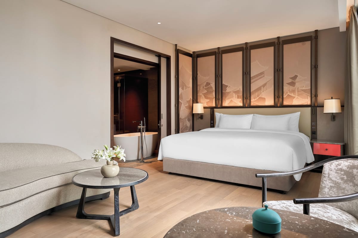 Une chambre d’hôtel moderne avec un grand lit, un canapé, une petite table ronde ornée d’un vase de fleurs et une table de chevet rouge.