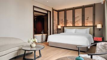 Une chambre d’hôtel moderne avec un grand lit, un canapé, une petite table ronde ornée d’un vase de fleurs et une table de chevet rouge.