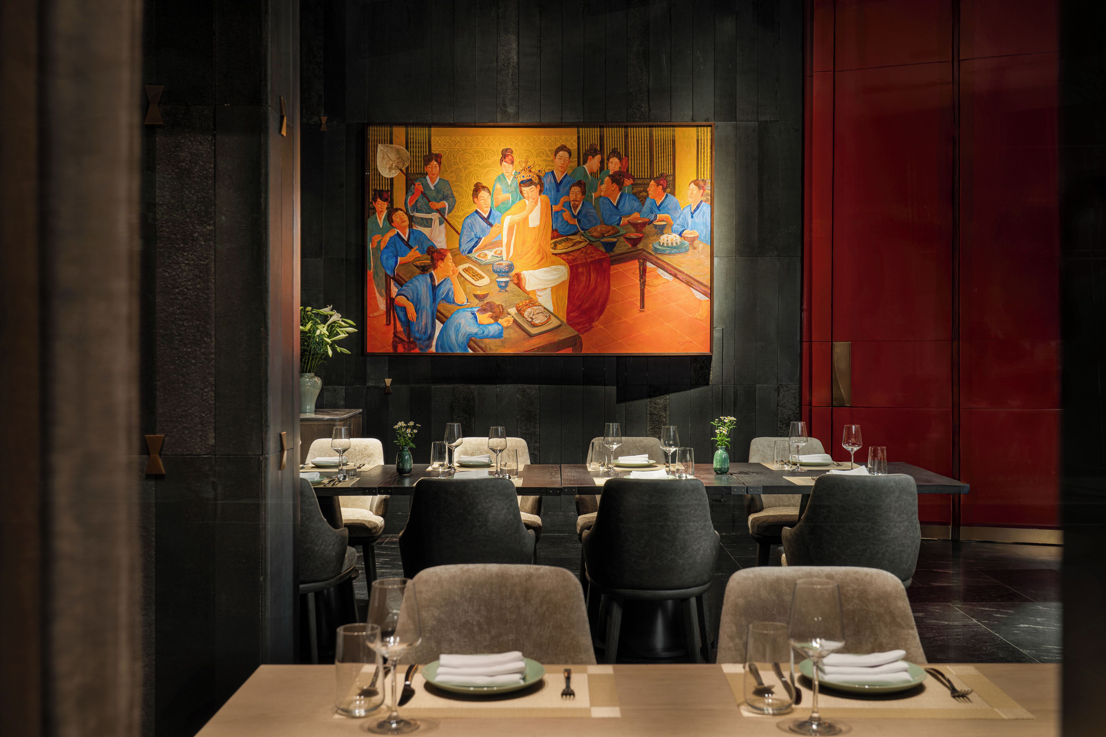 Comedor con una gran pantalla de televisión que muestra una pintura, mesas dispuestas con platos y vasos, y sillas de tonos oscuros.