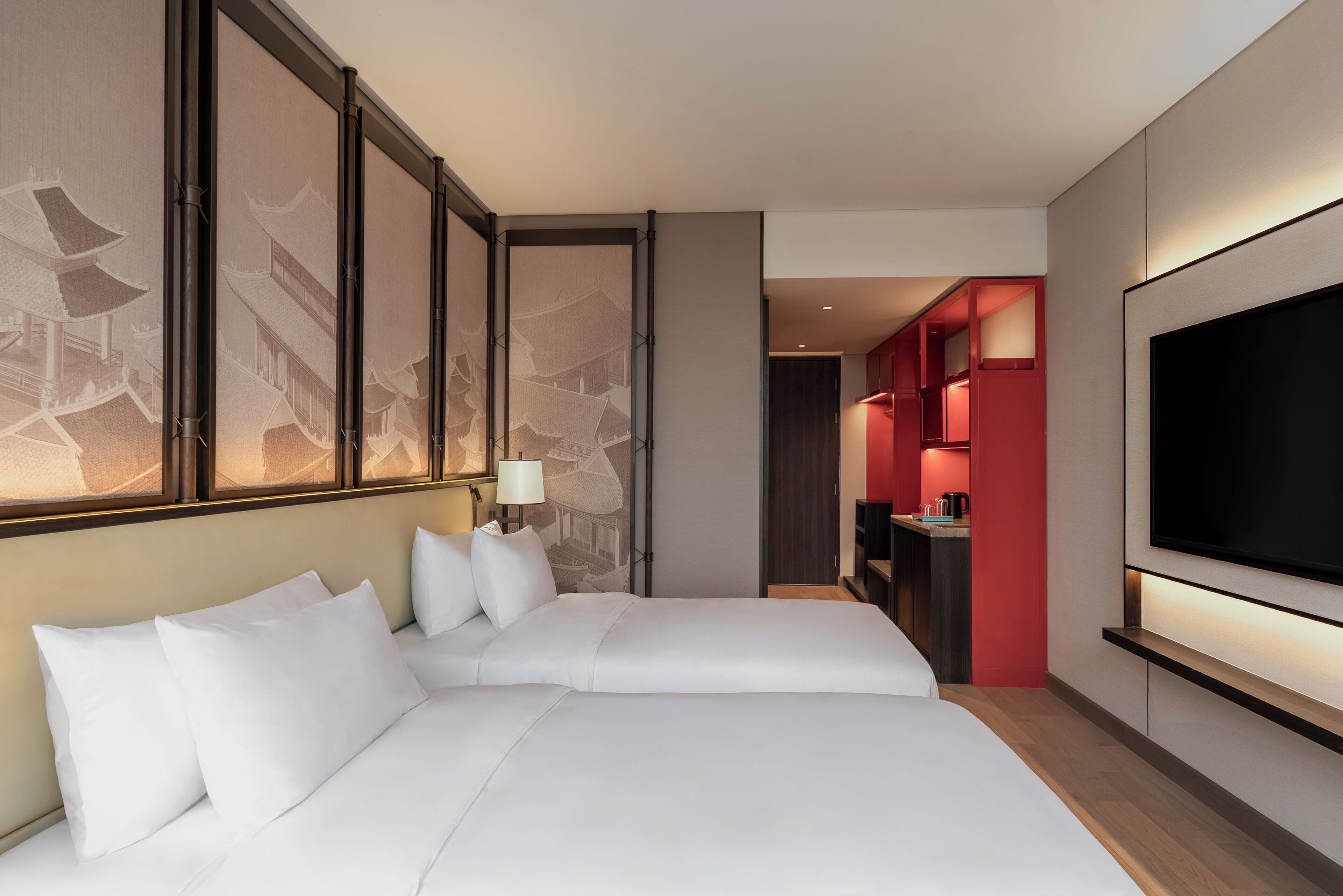 Habitación de hotel con una cama grande, televisión montada en la pared y una zona de comedor independiente con detalles en rojo.