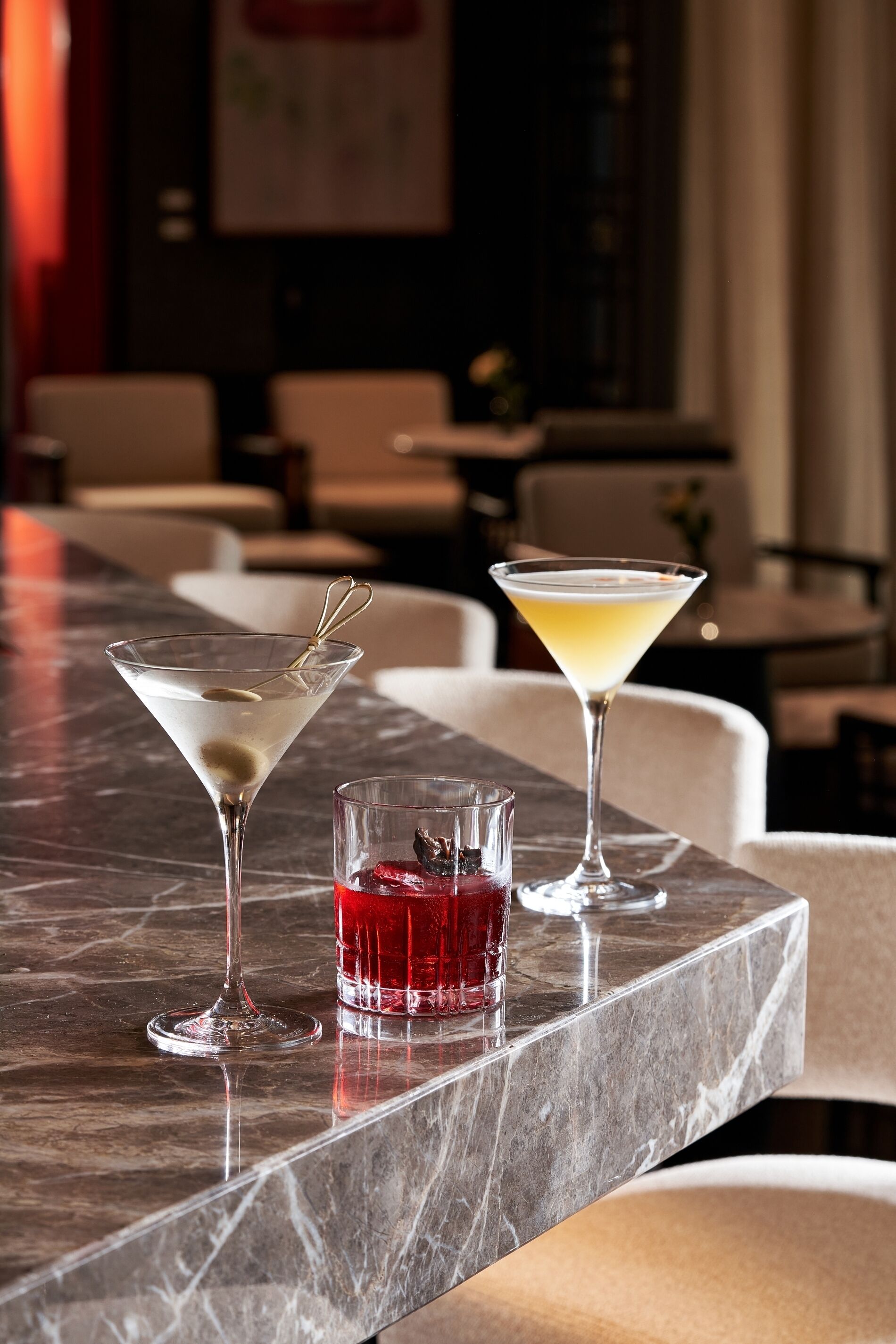 A bar area with a marble countertop, two martini glasses, and a small glass with a red drink.
